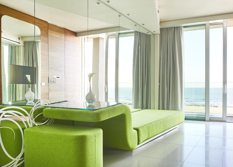 Salotto moderno con vista mare, arredi verdi e ampie vetrate.