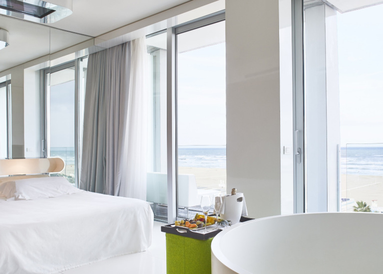 Camera moderna con vista mare, letto bianco e vasca rotonda.