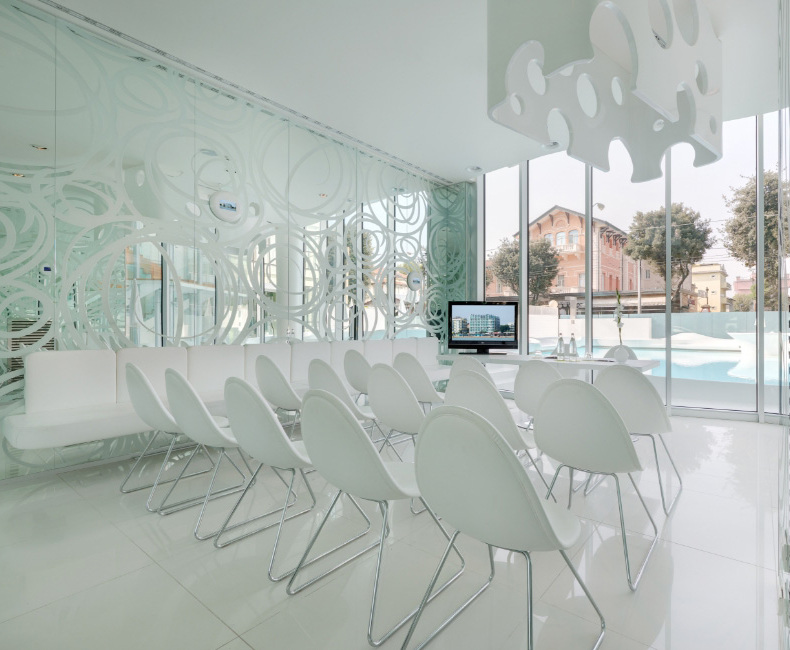Sala riunioni moderna con sedie bianche e pareti di vetro decorato.