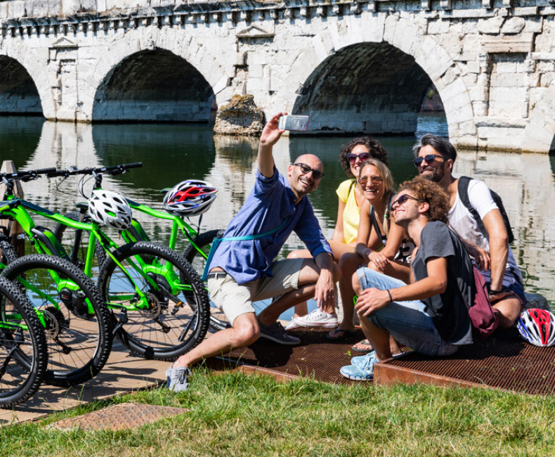 Glückliche Freundesgruppe macht Selfie mit grünen Fahrrädern vor antiker Brücke.