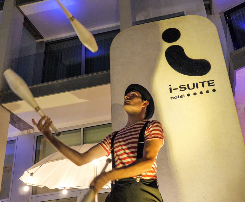 Giocoliere davanti all'hotel i-Suite, con luci colorate e atmosfera vivace.