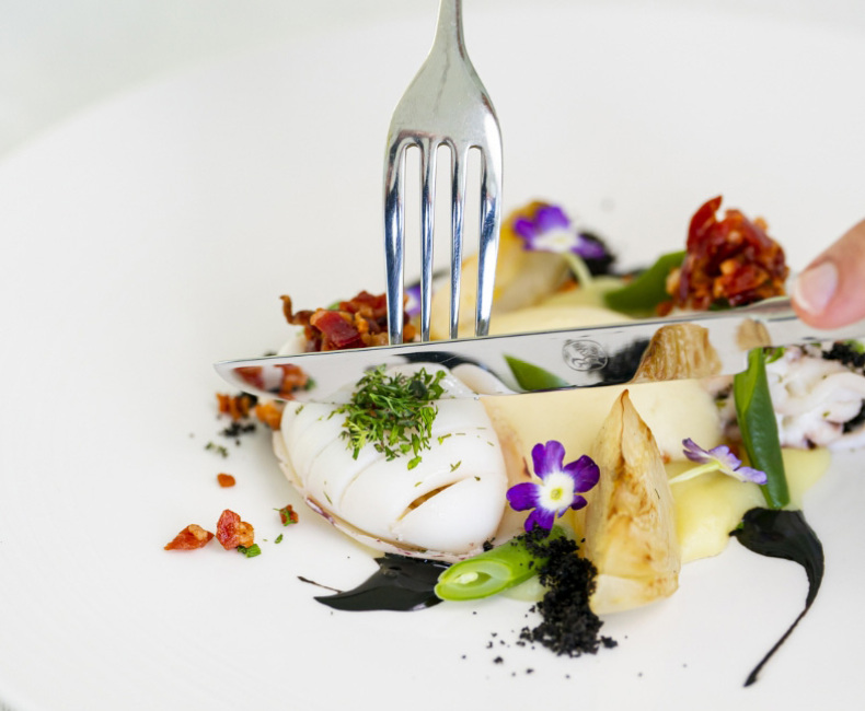 Piatto gourmet con calamari, verdure, fiori commestibili e decorazioni eleganti.