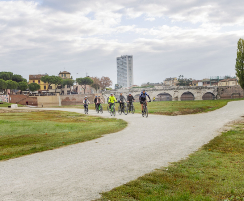 Ciclisti su un sentiero accanto a un ponte storico in una città italiana.